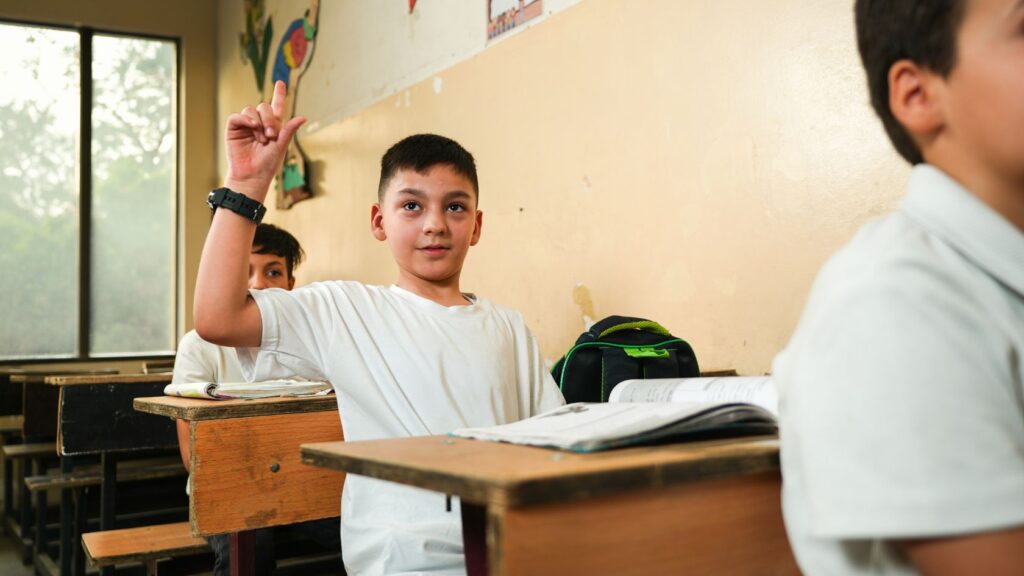 A schoolboy raising his hand to answer a question at his desk in a classroom